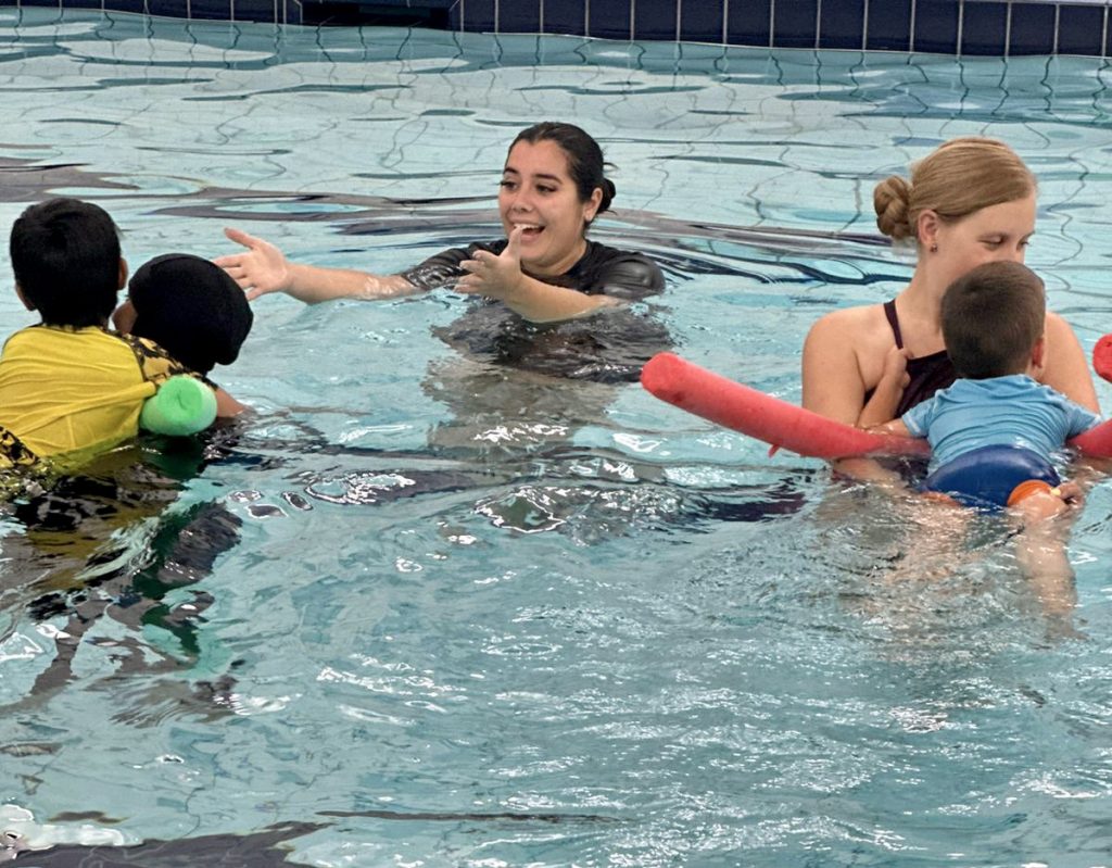 Love to Swim Swimming lessons in East London for all ages. Parents and toddlers enjoy a splash in the pool together. Instructor encourages a little one with outstretched arms.