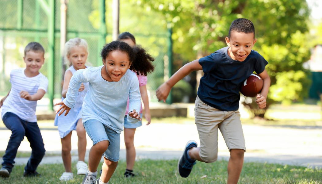 Children representing different ethnicities and genders have fun together running with a rugby ball. Rugby for kids in East London at Victoria Park