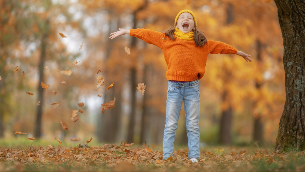 Girl wears orange in a forest of orange autumn leaves. She looks happy that it is autumn. Fun things to do in East London with kids this October