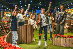 a multiracial group of children both boys and girls raise their arms enthusiastically while playing mini golf at Swingers Mini Golf Adventure