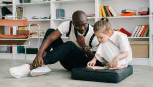 A man leans over supporting a child sitting on a cushion - will children lose 1-1 support in mainstream setting with EHCP reform