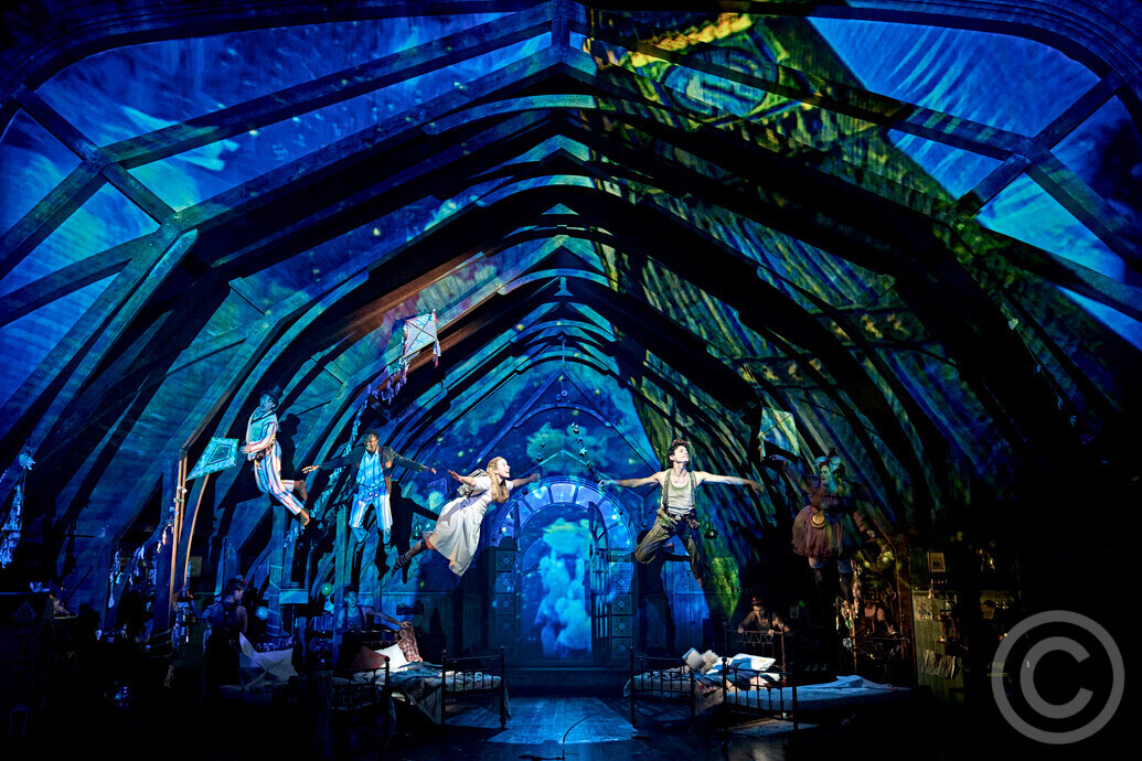 Scene from the Royal Shakespeare Company’s Wendy & Peter Pan at the Barbican, showing Wendy, Peter, and the Darling children flying through a magical blue-lit nursery on their way to Neverland.