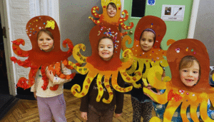 5 children wearing octopus costumes they have made themselves out of paper at the Art Imaginarium holiday camp smile at the camera. Proud of their creations