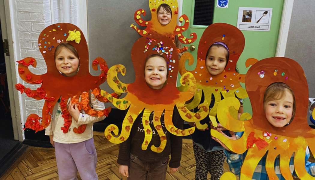 5 children wearing octopus costumes they have made themselves out of paper at the Art Imaginarium holiday camp smile at the camera. Proud of their creations