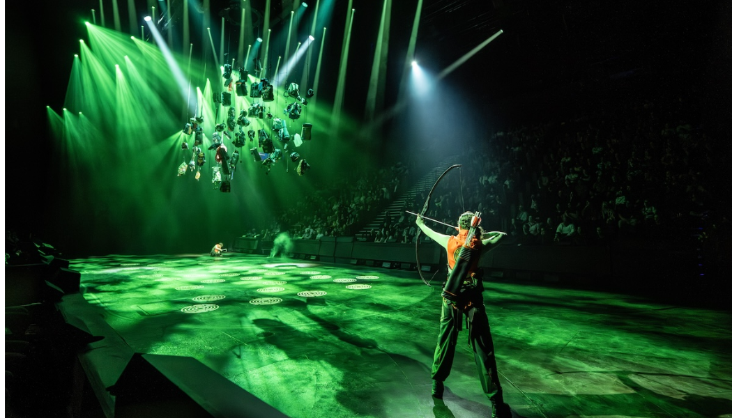 Catniss stands in a green lit stage and points her arrow her back to us. Image is taken from Hunger Games live one of the events chosen in our March round up of things to do in East London with kids