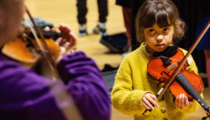 Young girl focuses on her teacher as she learns to play the violin at The Strings Club half term in East London