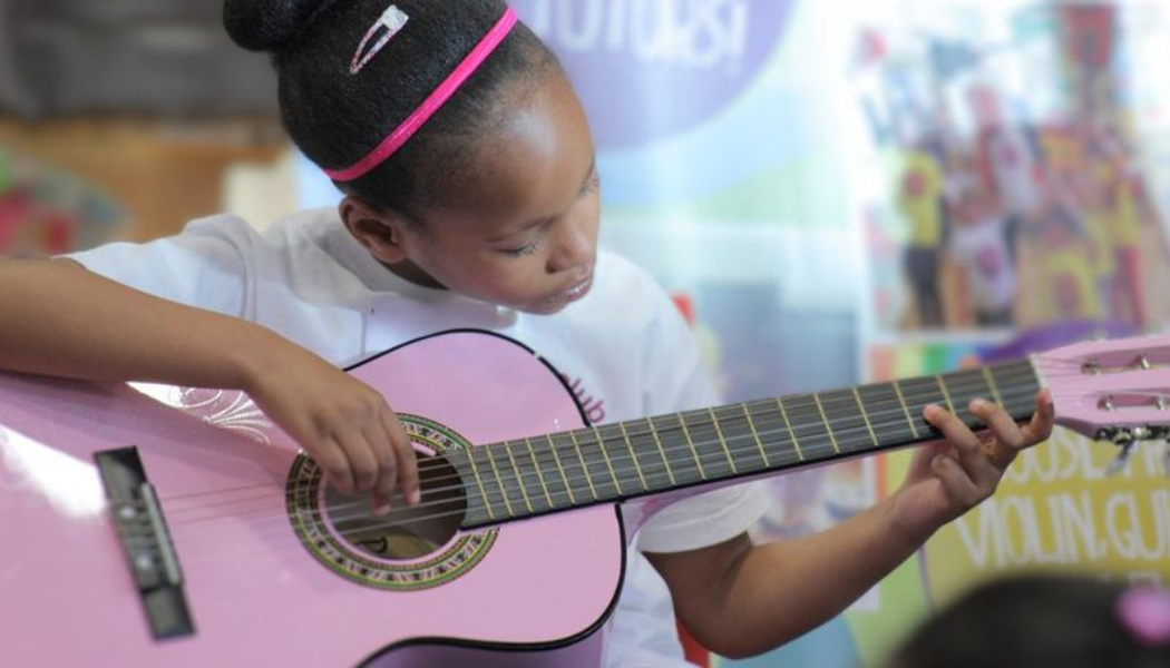 Young girl learning to play a pink guitar during one of Strings club's Half Term camps in East London